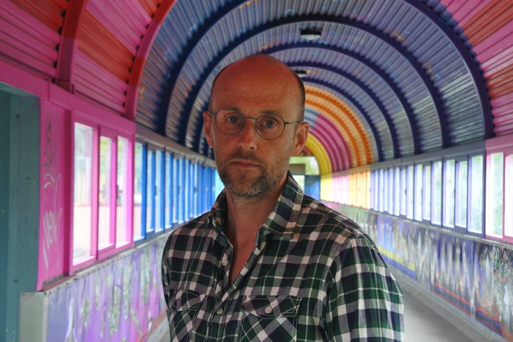 Halvbild på Pelle Sunvisson som står i en färgglag tunnel. 