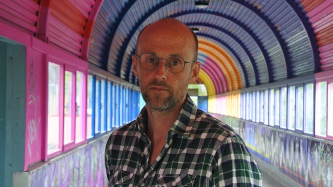 Halvbild på Pelle Sunvisson som står i en färgglag tunnel.