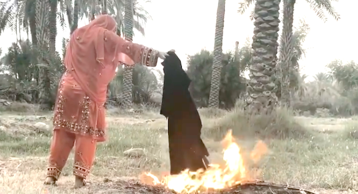 Kvinna står utomhus och eldar upp en hijab, ett täckande klädesplagg.