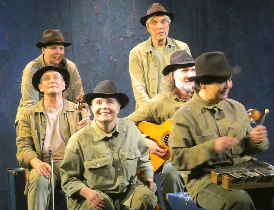 Sex personer som är skådespelare har på sig gröna arbetskläder och hatt, alla likadant klädda och spelar samma roll som Joe Hill. Flera personer håller i instrument