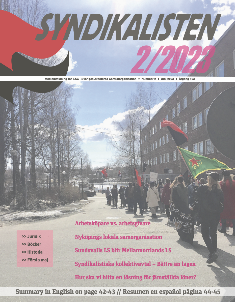 Framsida till tidningen Syndikalisten, nummer 2 2023. I bakgrunden ett foto från Första-maj-demonstration i Umeå.