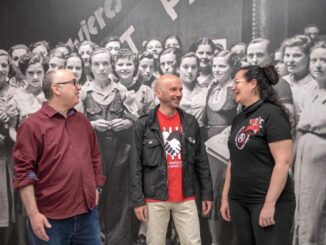 Foto som visar representanter från tre anarkosyndikalistiska fack i Spanien. I bakgrunden en stor svartvit bild med massa kvinnor