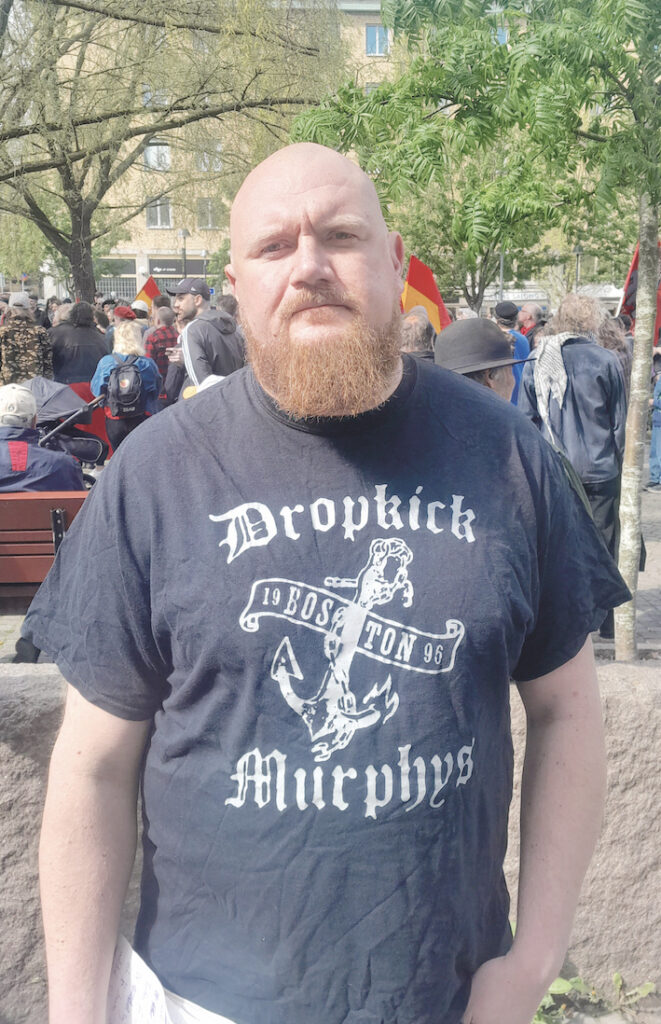 Erik Helgeson, vice ordförande i Hamnarbetarförbundet. I bakgrunden syns en samling för Första maj-firande samt grönska.