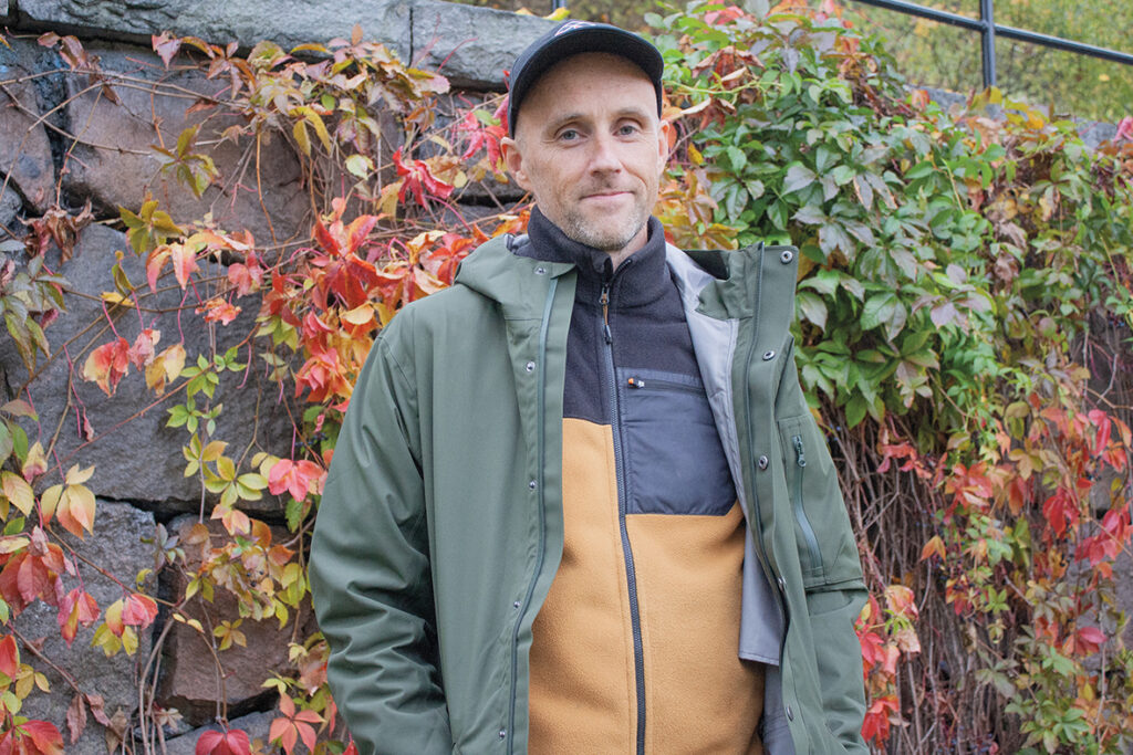 Pelle Sunvisson står framför en mur med höstfärgad växtlighet.
