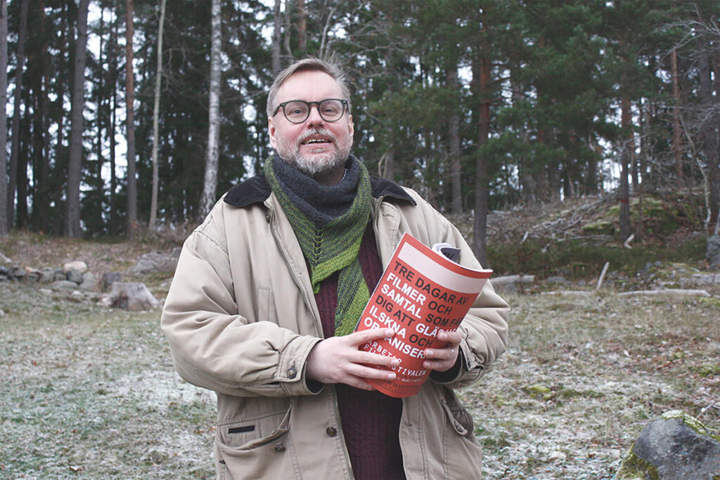 SAC:s nye informationsorganisatör och redaktör för Syndikalisten står i ett senhöstlandskap och håller ett nummer av Syndikalisten i handen.